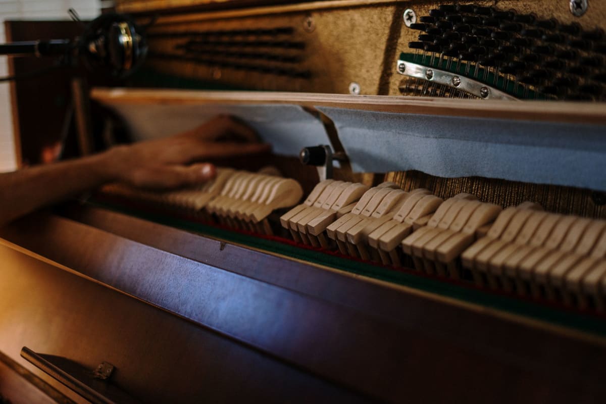Technician’s hand adjusting the wooden action inside an upright piano