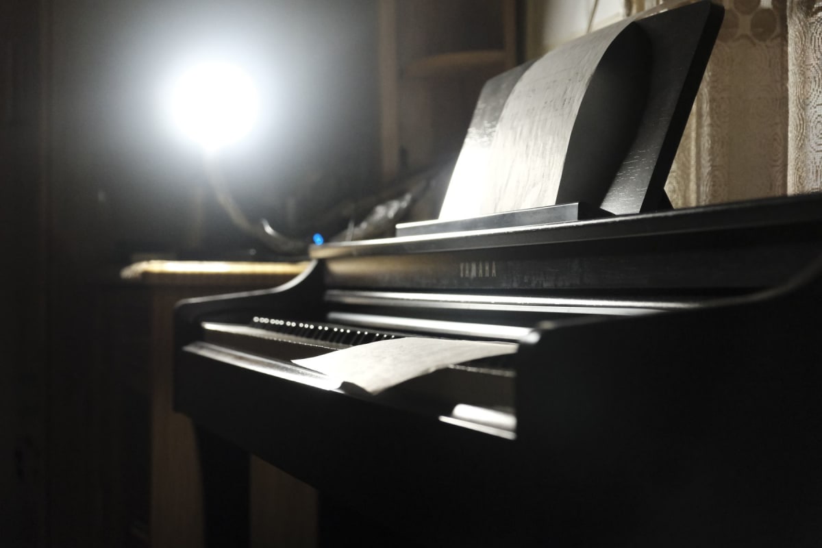 Bright exposed lamp creating glare beside sheet music on a black upright piano