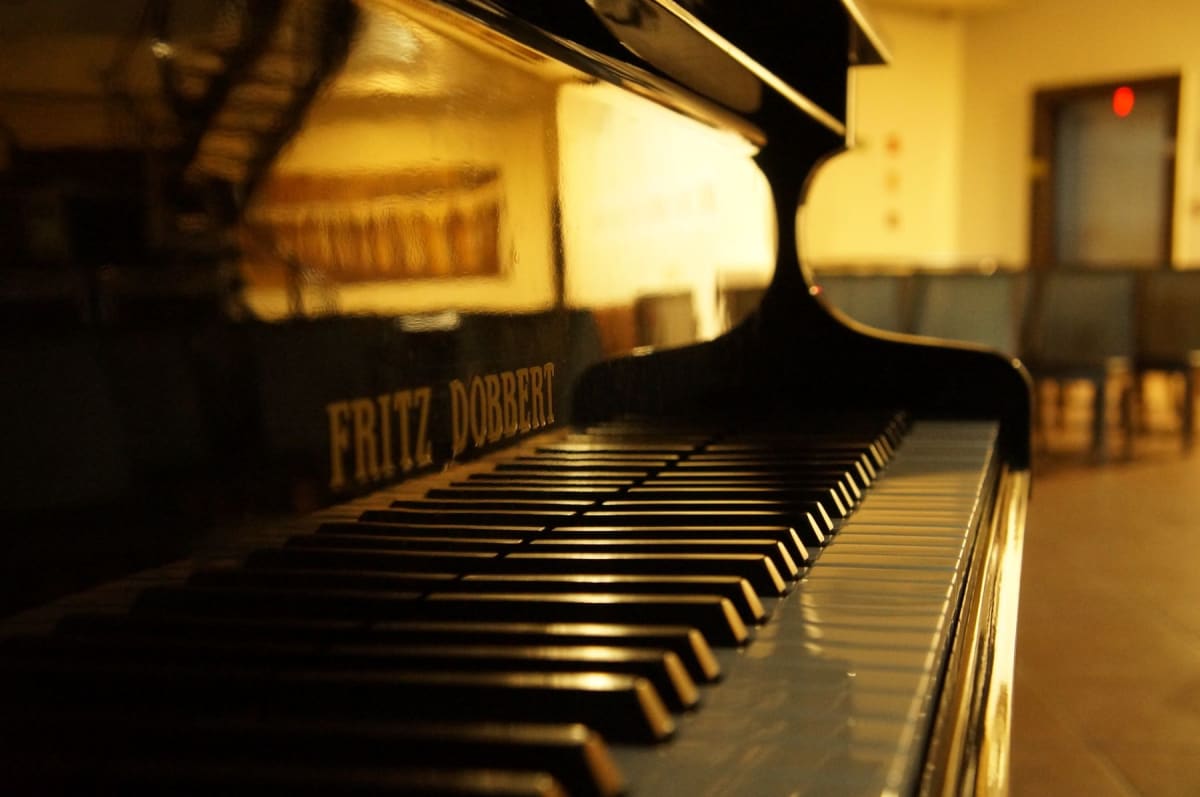 Warm room lights reflected across a glossy black grand piano and its keyboard