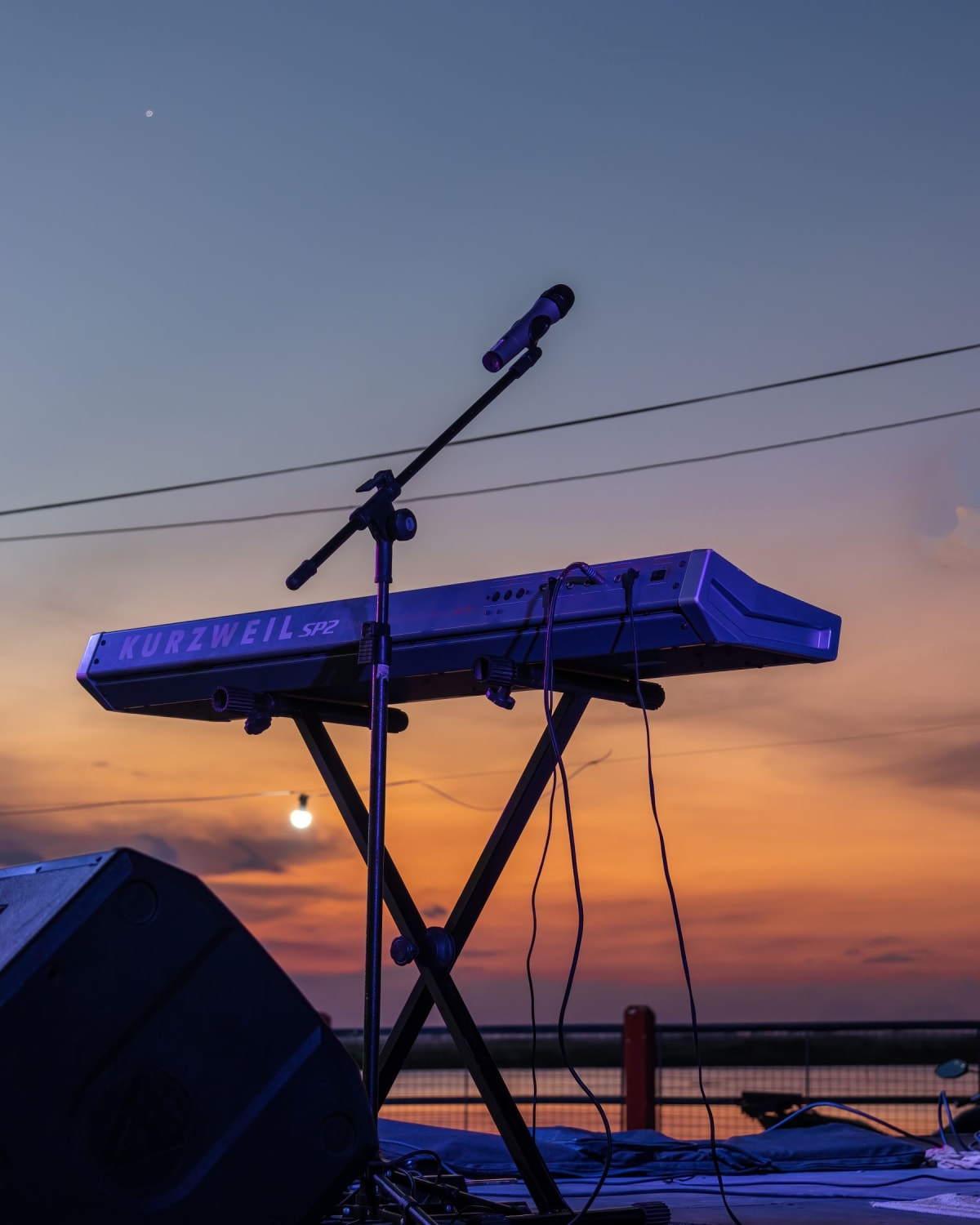 Portable keyboard and microphone set up on an outdoor stage at sunset