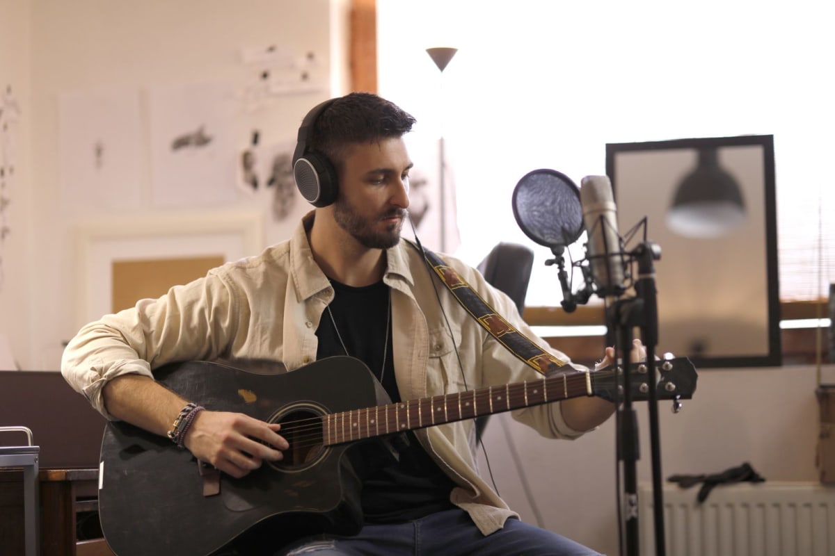 Guitarist wearing headphones while recording beside a studio microphone