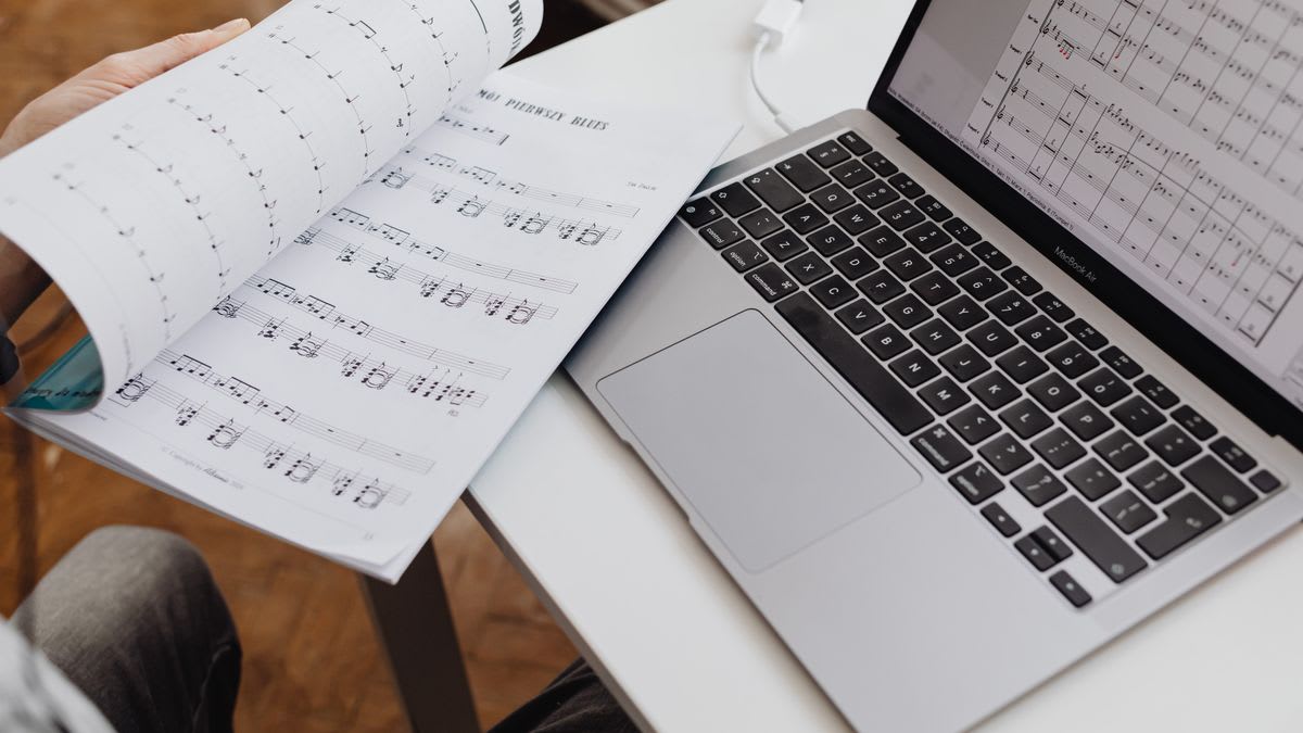 Printed sheet music open beside notation displayed on a laptop