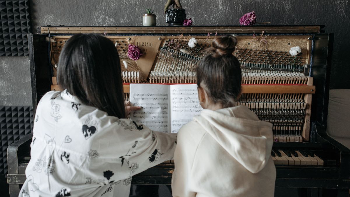 A teacher and student reading music together at an upright piano