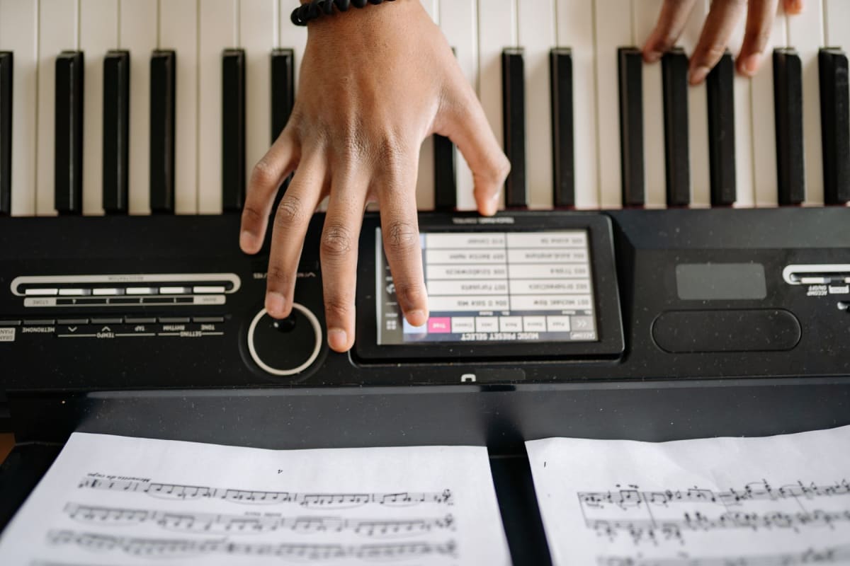 Overhead view of hands playing an electronic keyboard above open sheet music