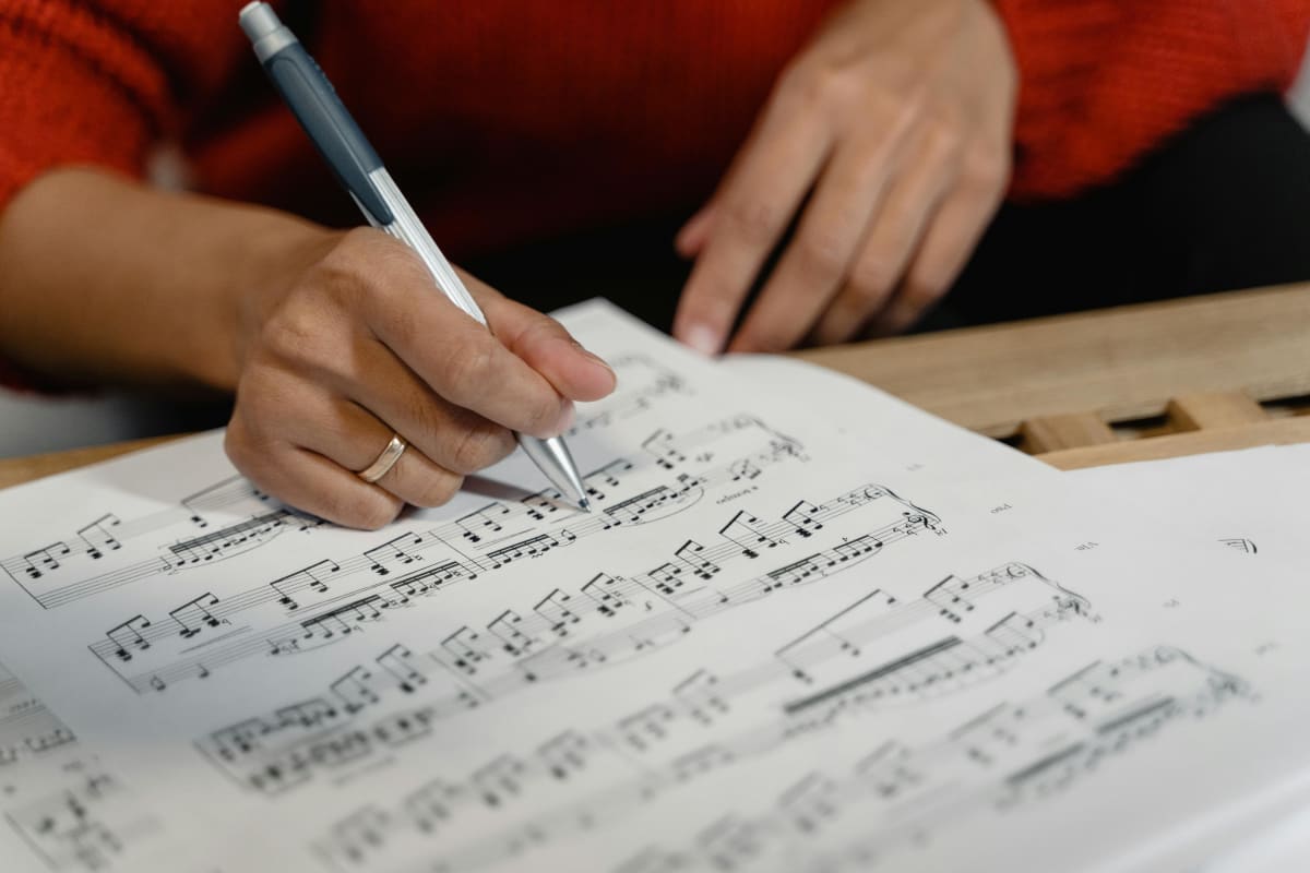 Close-up of a person writing notes on sheet music during review
