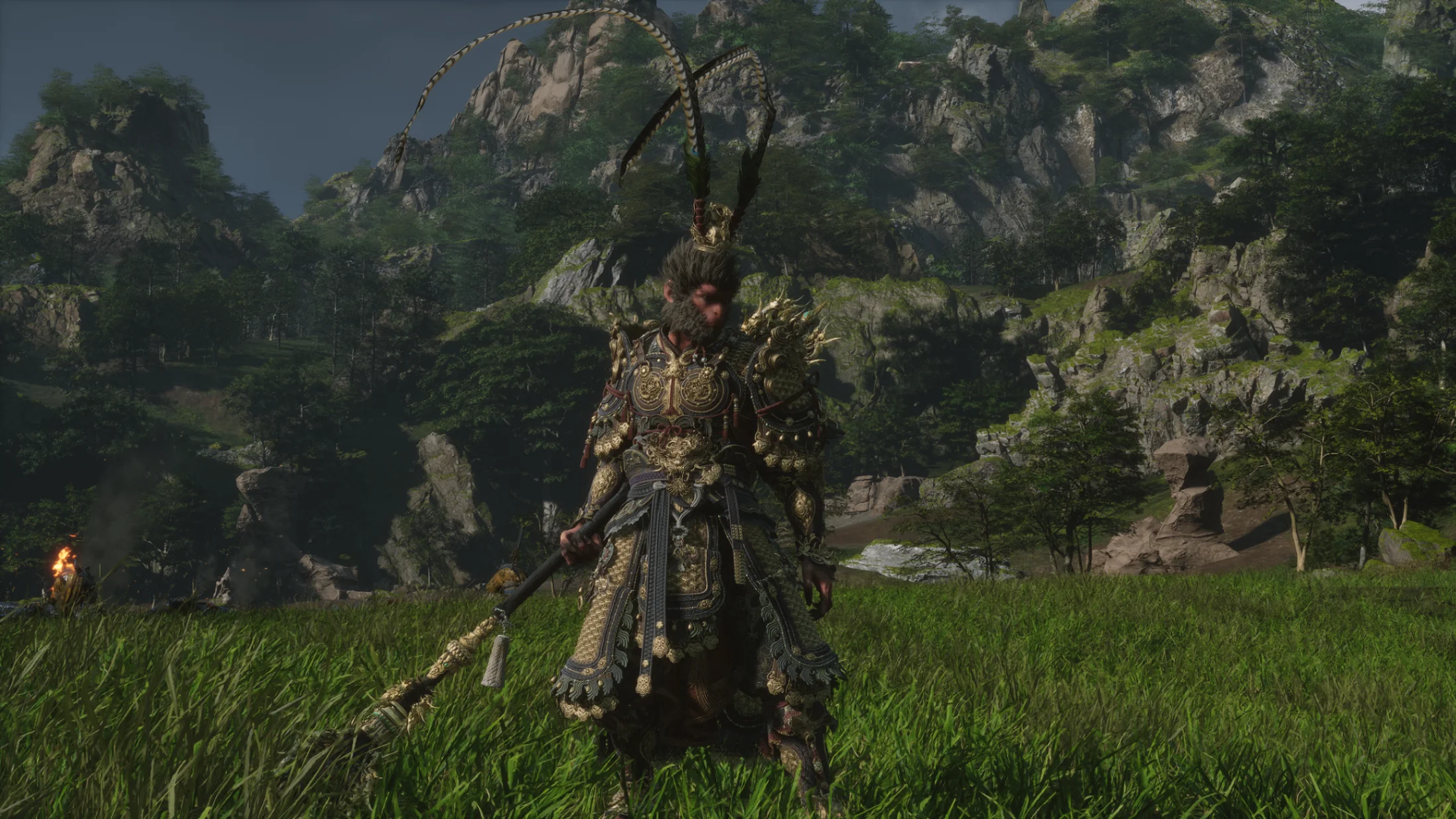 The Destined One stands in a grassy valley surrounded by towering mountains in Black Myth: Wukong.