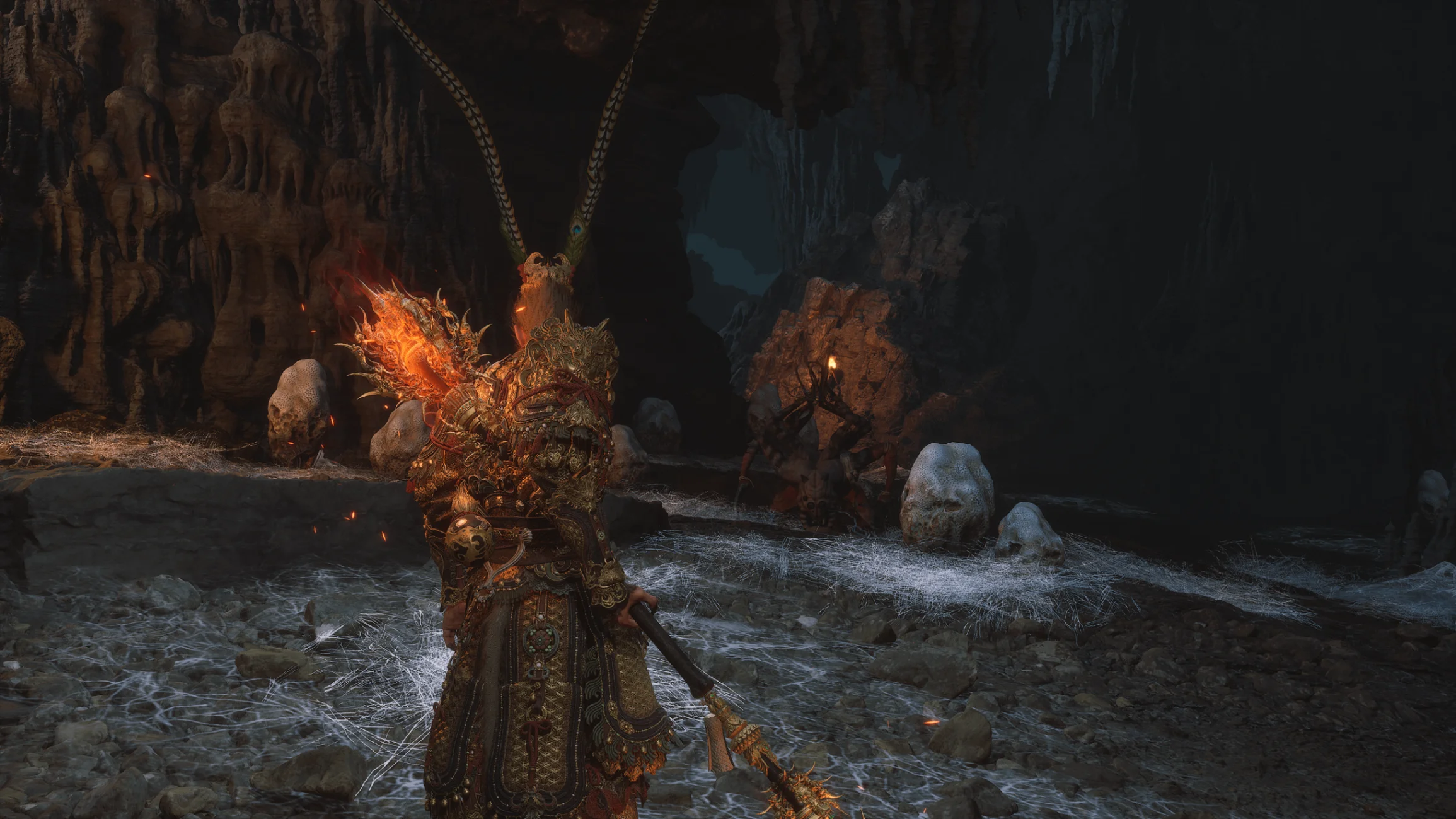 The Destined One explores a dark cavern covered in webs while wielding a flaming staff in Black Myth: Wukong.