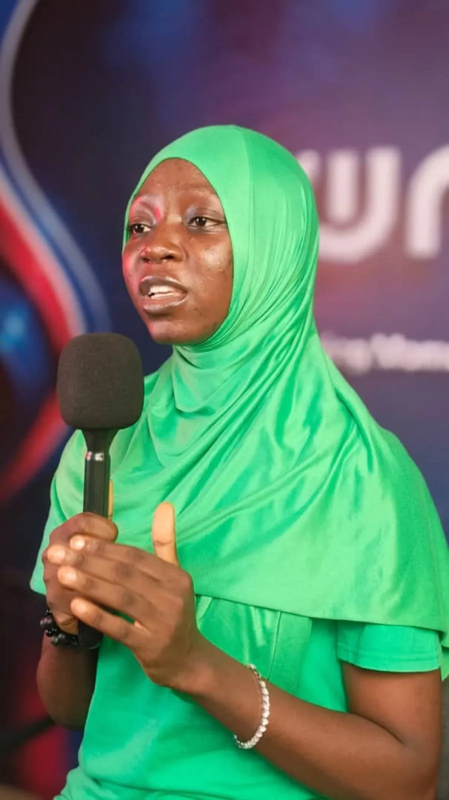 Guest in a green hijab speaking with a microphone