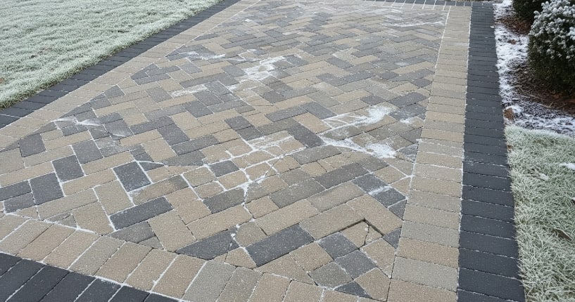 Patterned stone driveway with light frost and scattered patches of snow on a cold winter morning.