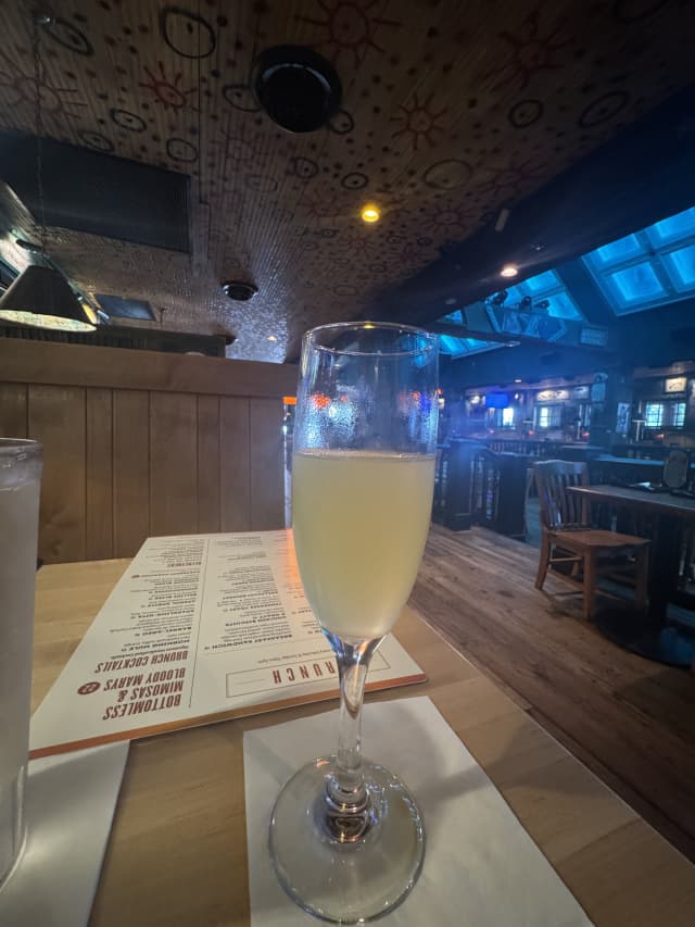 Bottomless mimosa in a wine glass on a wooden table with the House of Blues brunch menu visible and the blue-lit dining room at Disney Springs in the background