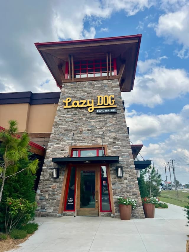 Stone entrance tower of Lazy Dog Restaurant & Bar in Kissimmee with its yellow Lazy Dog Eat Drink sign under a blue sky