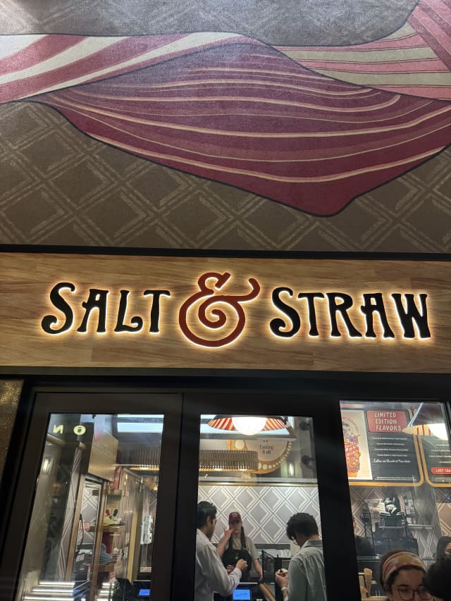 Salt & Straw illuminated storefront sign with swirled ice cream mural at Disney Springs West Side, guests visible inside through the windows