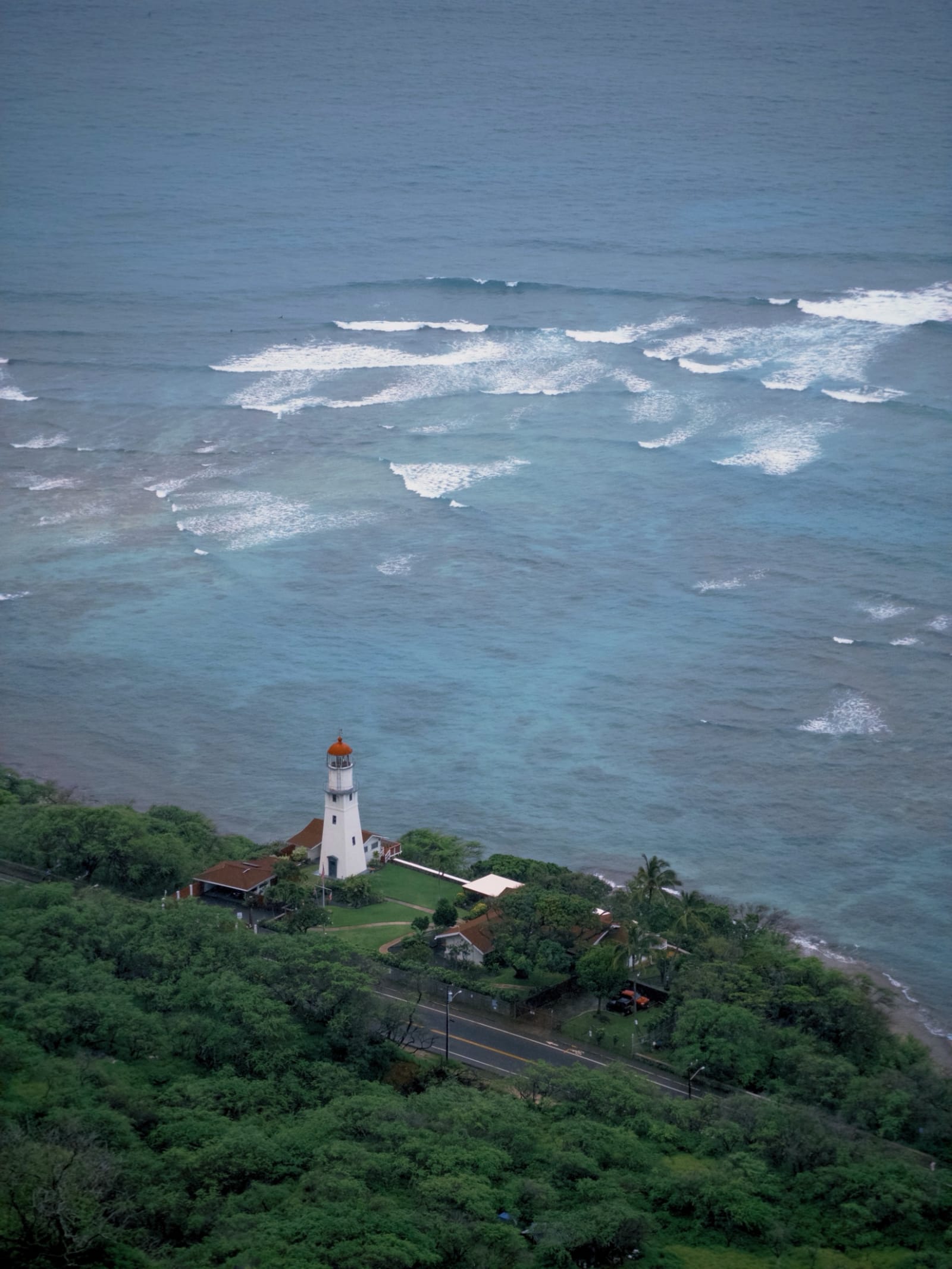A white lighthouse on a green headland above a churning sea