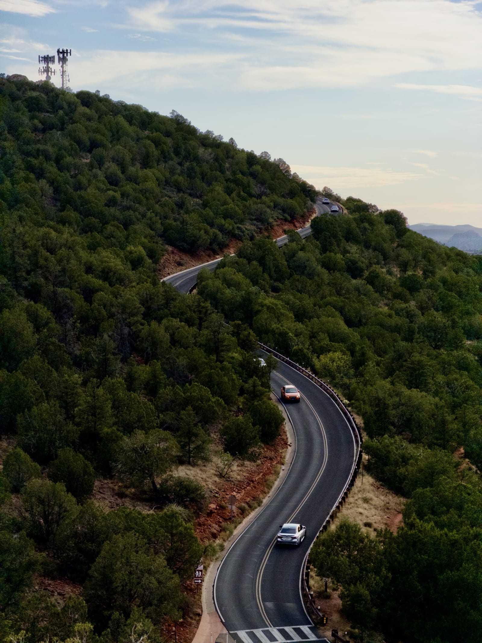 A car on a hairpin road cut into a forested mountainside