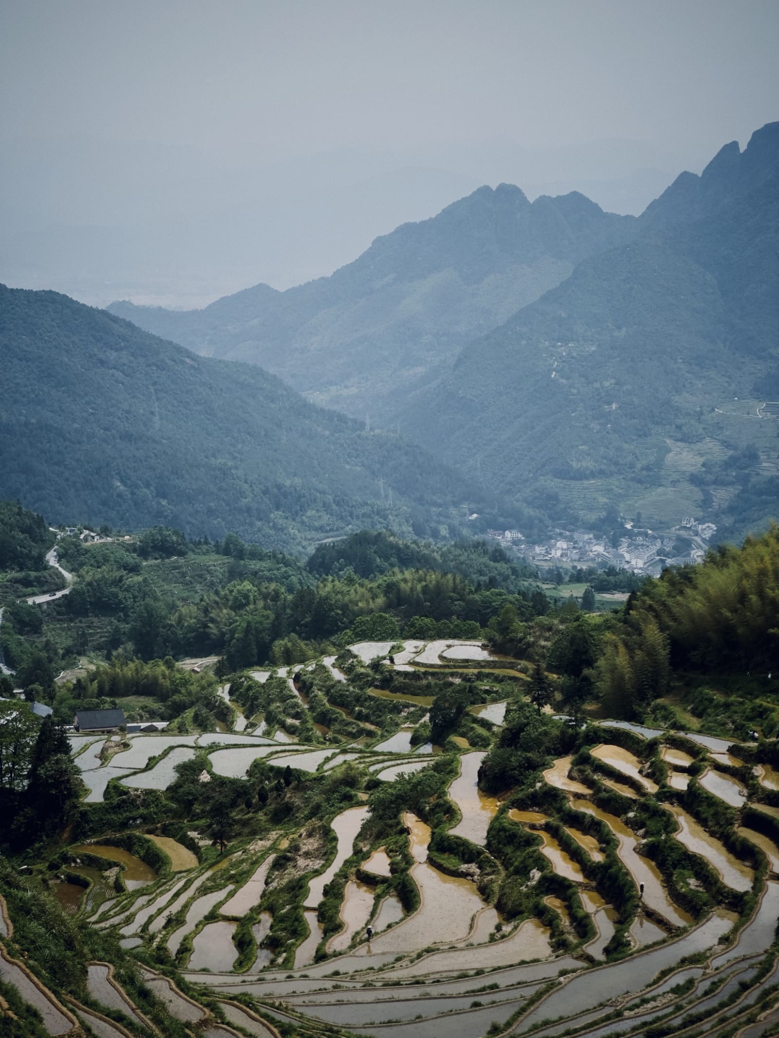 Terraced paddies stepping down a misty mountain valley toward a village
