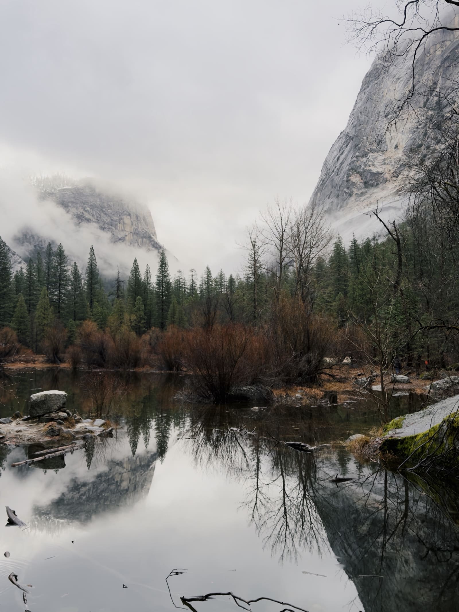 A granite valley under low cloud, reflected in a still river