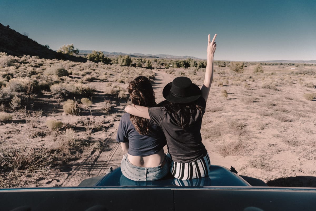 Two vacation buddies sitting on a car in the desert.