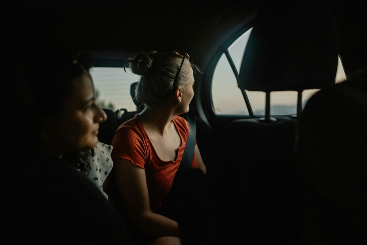 two girls sat in a car looking out of the window 