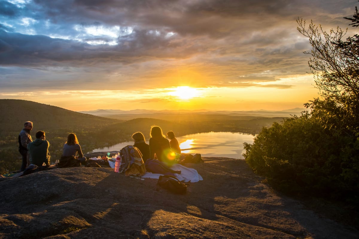 Reisepartner gesucht und gefunden, Gruppe macht ein Picknick bei Sonnenuntergang auf einem Berg vor einem klaren See