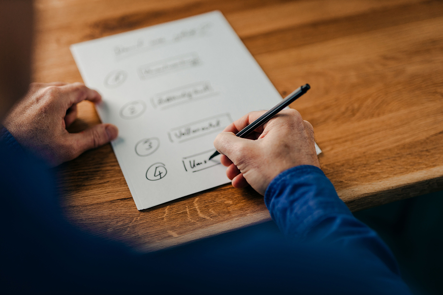 Someone writing a numbered list of four steps by hand on paper at a wooden desk