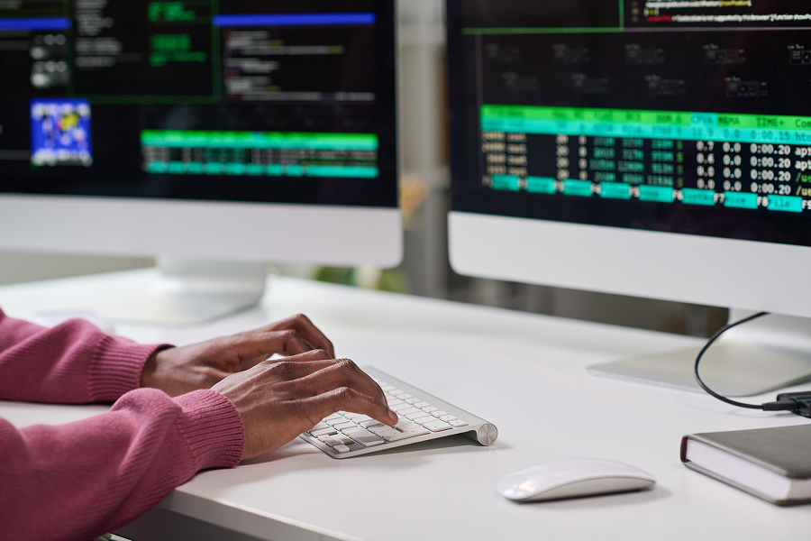 Hands typing on a keyboard at a desk with two monitors