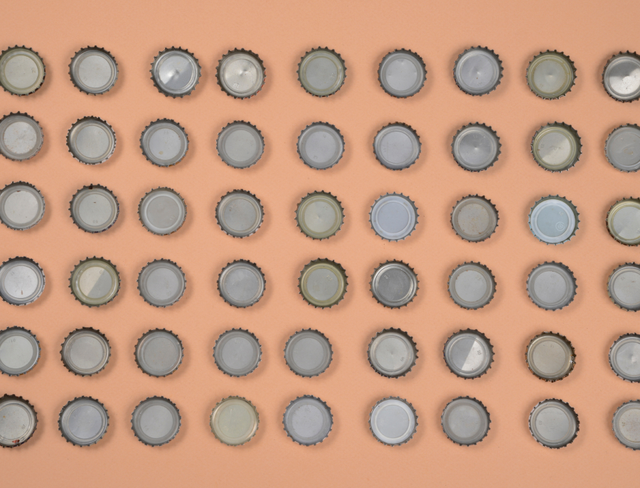 Rows of identical metal bottle caps arranged in a regular grid on a plain peach background