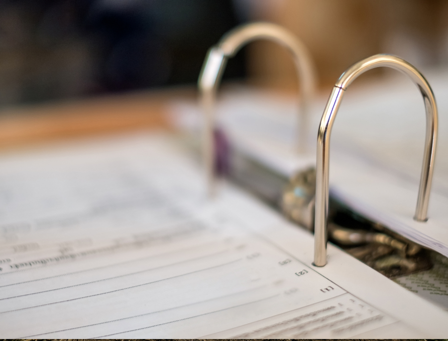 An open ring binder of printed forms photographed close up, with the metal rings sharp and the pages falling away out of focus