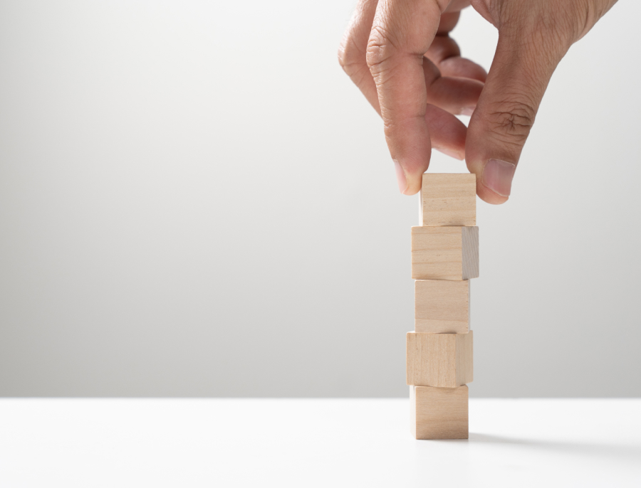A hand placing a wooden block on top of a short stack of blocks on a white surface