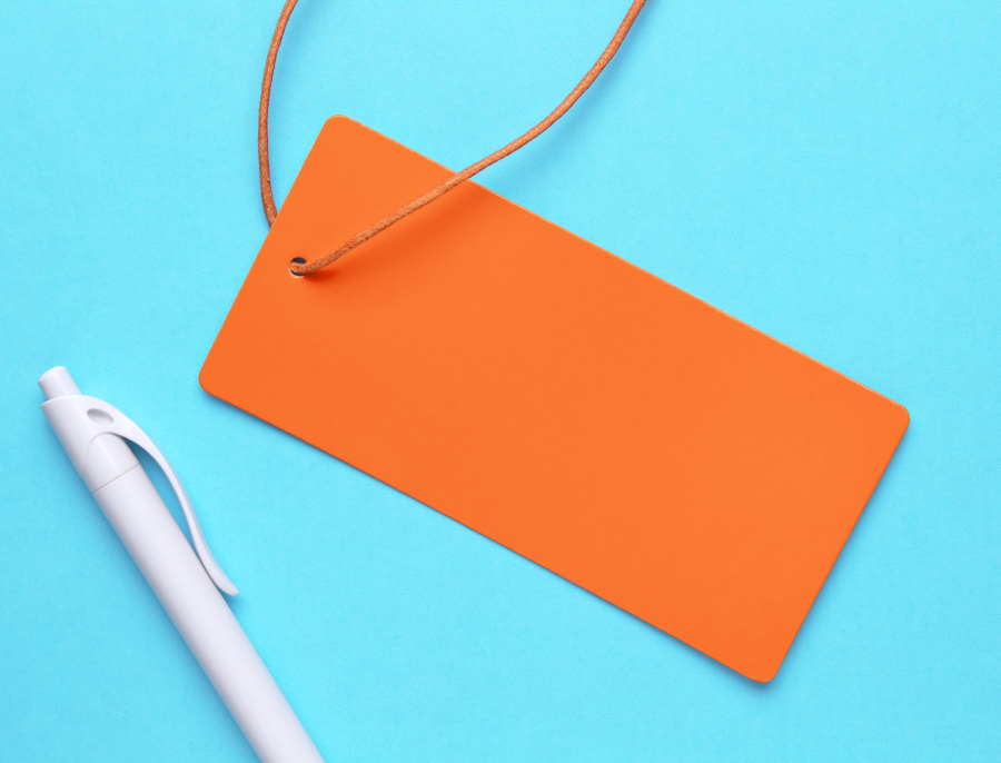 A blank orange price tag on a string lying on a bright blue surface next to a white pen