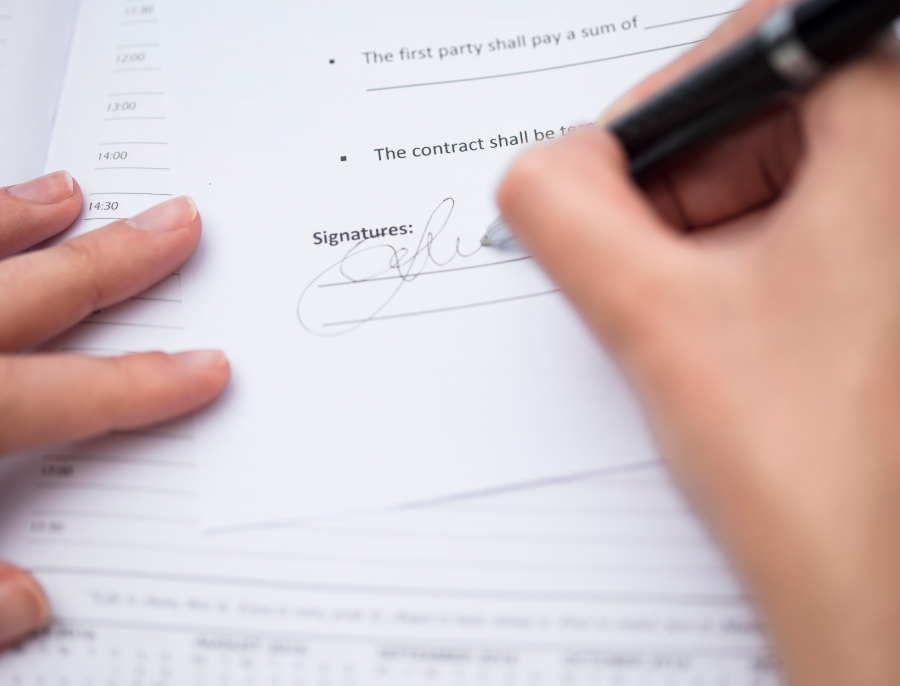 Close up of a hand signing the signature line of a printed contract