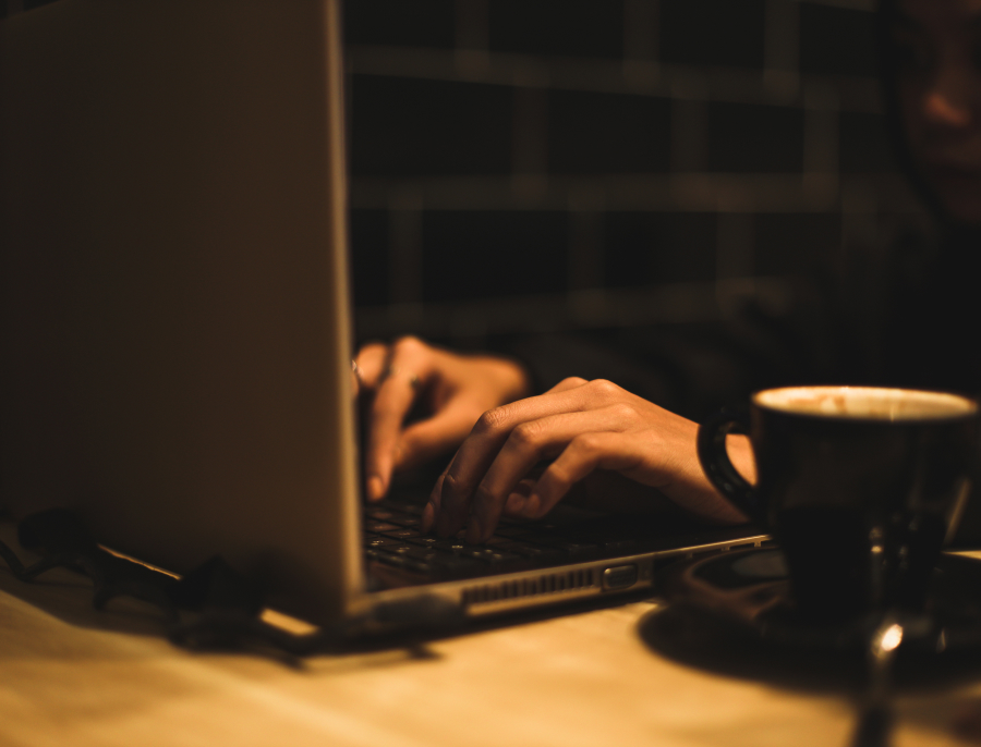 Hands typing on a laptop keyboard in low warm light, a cup of coffee beside the machine