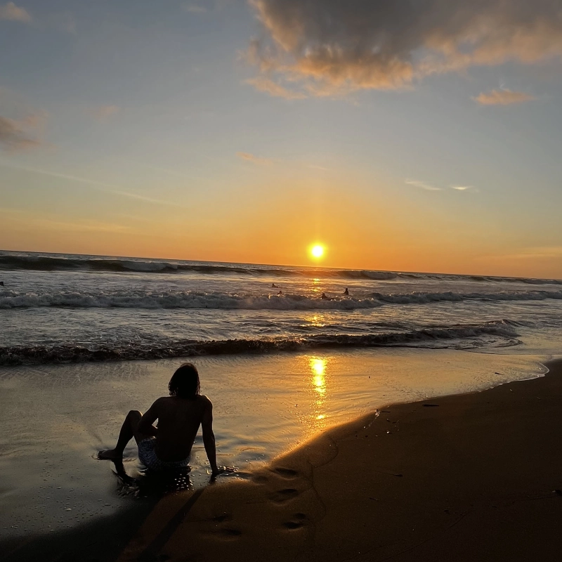 Hombre sentado en la orilla de la playa viendo el atardecer