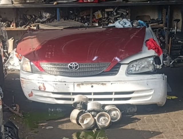 Toyota Corolla sedan front cut — maroon hood, white bumper, grille and headlights, Sharjah market