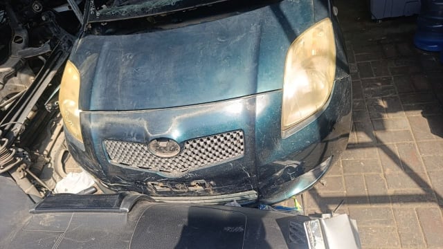 Dark green Toyota Yaris hatchback front cut — hood, bumper, grille and yellowed headlights, Sharjah market