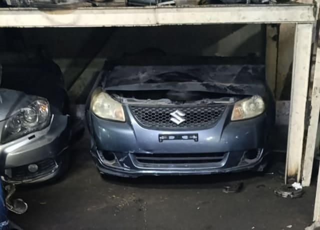 Grey-blue Suzuki SX4 sedan front cut — bumper, mesh grille and headlights, Sharjah market