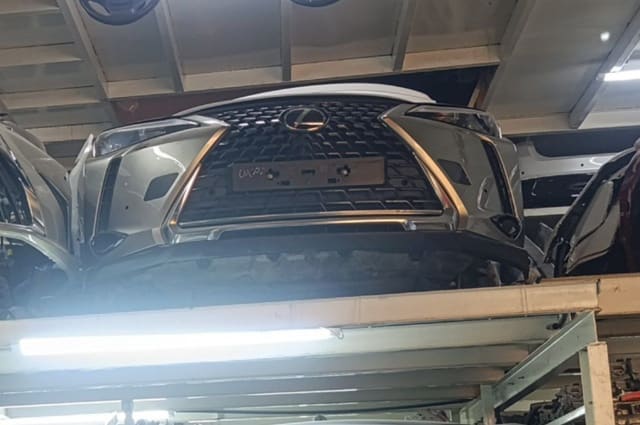 Silver Lexus NX SUV front cut — spindle grille and front bumper on a storage rack, Sharjah market