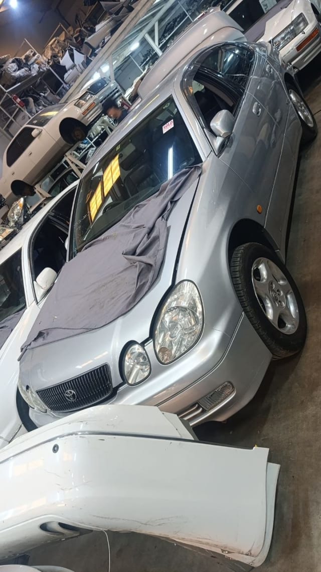 Silver Toyota Aristo car for parts on its side — front bumper, grille, headlights and alloy wheel, Sharjah market