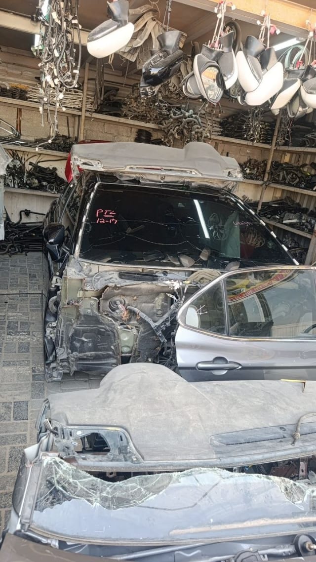 Dark grey Toyota Prius halfcut — exposed engine bay, firewall and windshield among stacked parts, Sharjah market