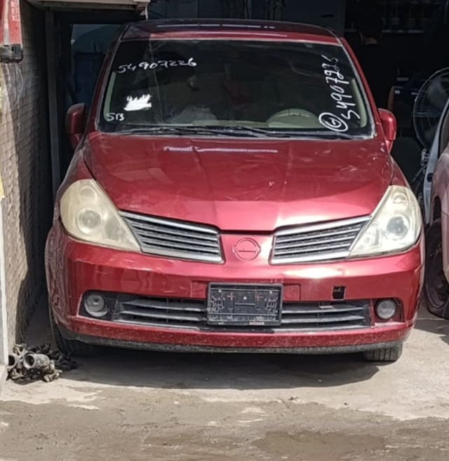 Red Nissan Tiida hatchback front — bumper, grille, headlights and hood, Sharjah market