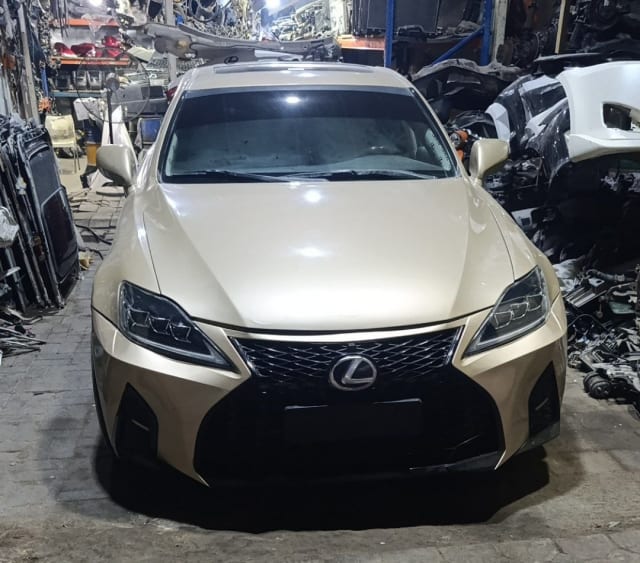 Gold Lexus IS sedan front cut — spindle grille, headlights, bumper and hood, Sharjah market