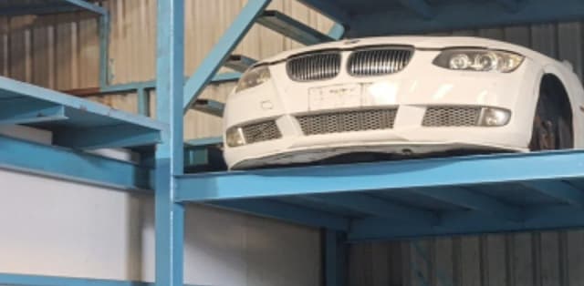 White BMW 3-Series coupe front halfcut on a blue rack showing bumper, kidney grille and headlights, Sharjah