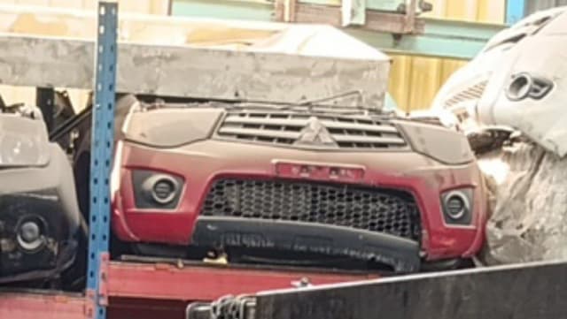 Red Mitsubishi L200 pickup front halfcut — bumper, grille and fog lights on a rack, Sharjah market