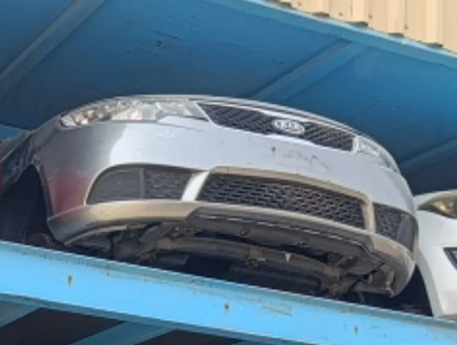 Silver Kia Cerato halfcut front end with bumper, grille and headlights on a rack, Sharjah market