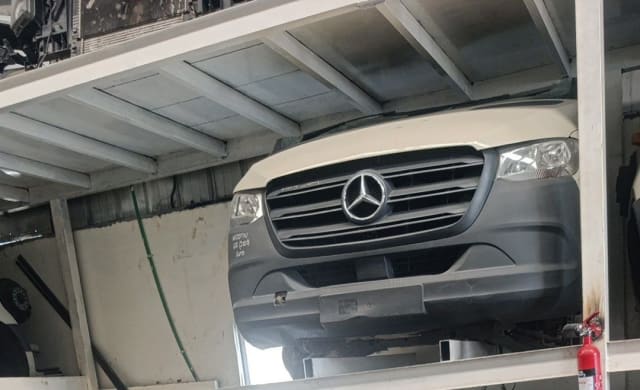 Cream Mercedes-Benz Sprinter van halfcut on rack — hood, grille, headlights, grey bumper, Sharjah market