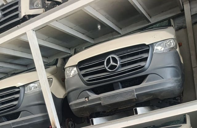 White Mercedes-Benz Sprinter halfcut on rack: grille, headlights, hood and grey bumper, Sharjah market