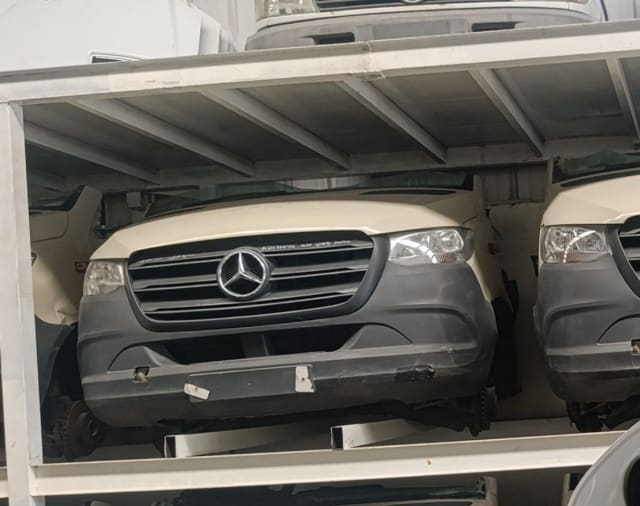Beige Mercedes-Benz Sprinter van front halfcut on a rack — hood, grille, headlights, bumper, Sharjah market
