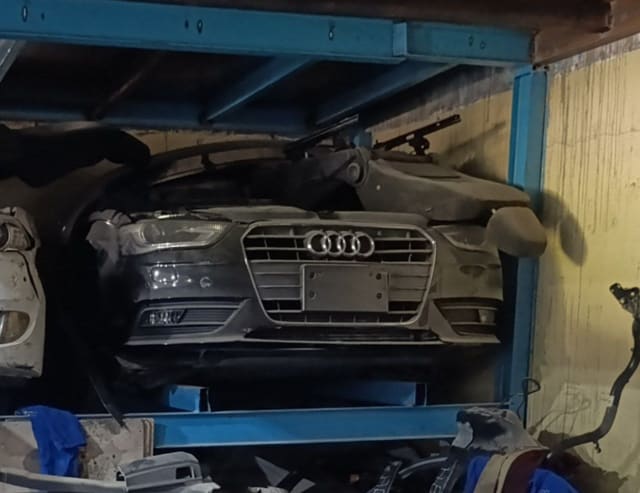 Dark Audi A4 front halfcut with bumper, grille and headlights on a blue rack, Sharjah market