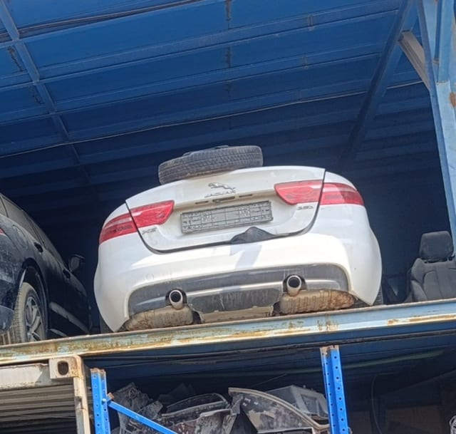 White Jaguar XE rear halfcut — trunk lid, taillights, bumper and twin exhaust on a rack, Sharjah market