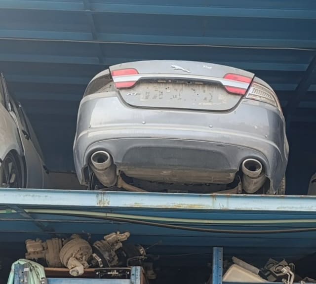 Grey Jaguar XF sedan rear: trunk lid, tail lights, bumper and twin exhausts on a rack, Sharjah market