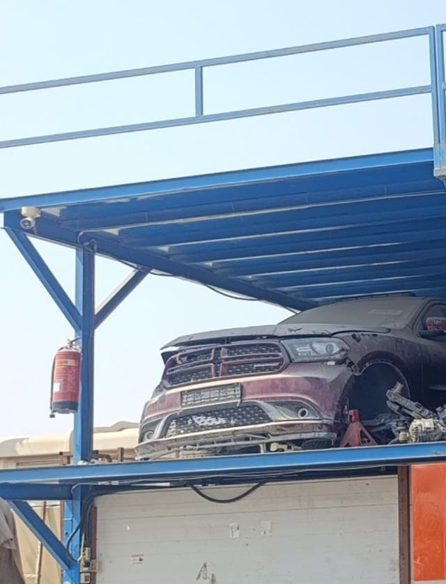 Dark red Dodge Durango car for parts on a storage rack, bumper, grille and headlights visible, Sharjah market